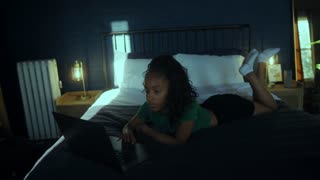 Handheld shot of woman lying in bed browsing on laptop